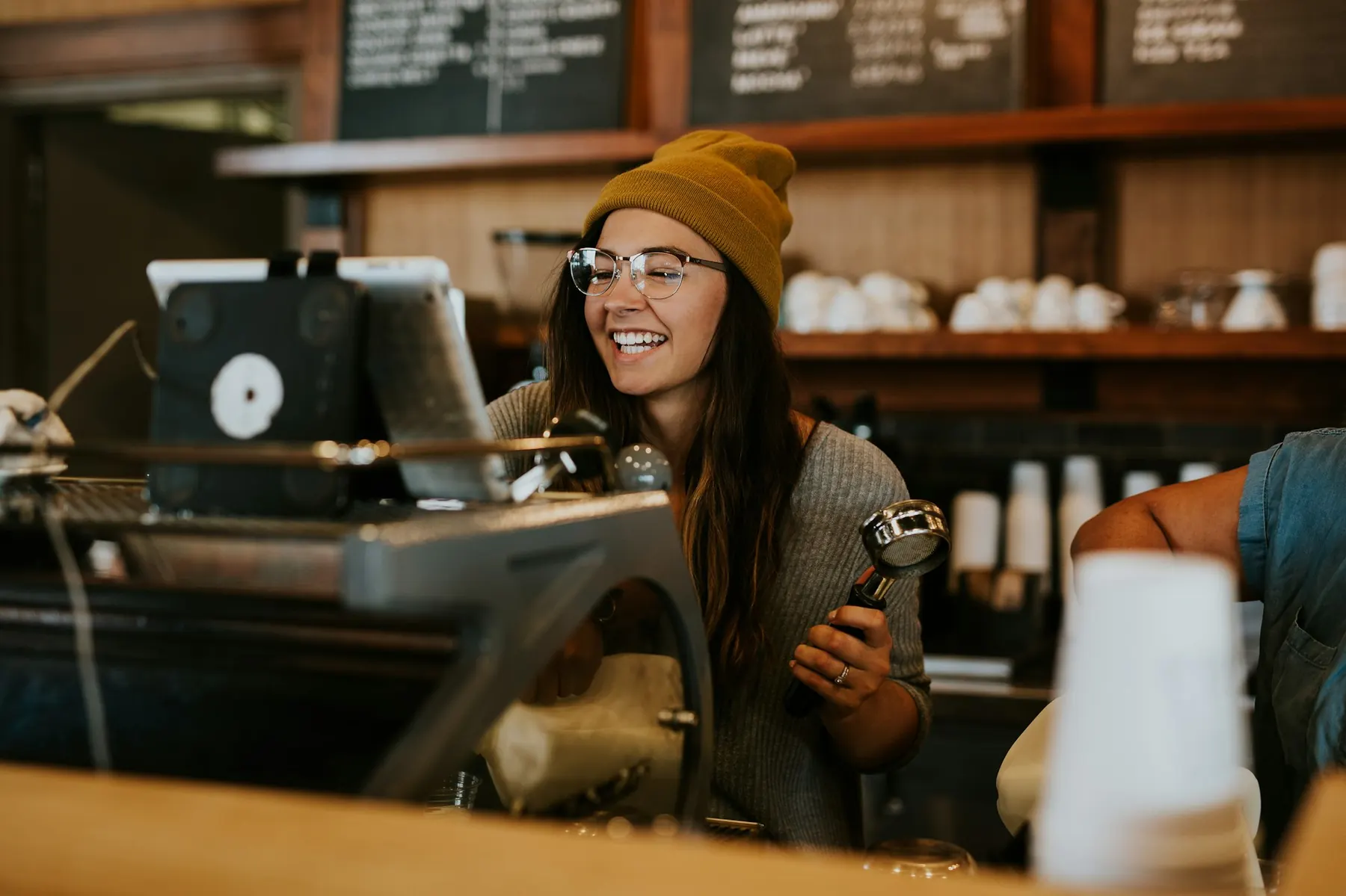En barista smiler bag espressomaskinen på en travl café.