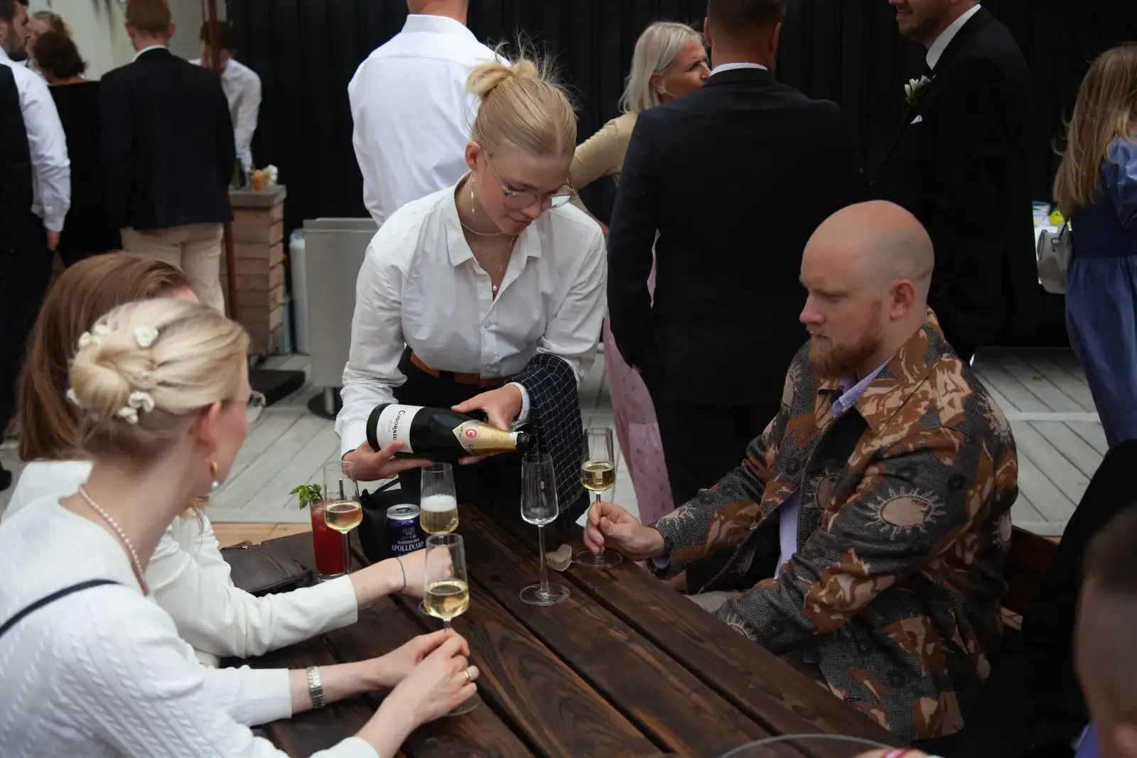 En tjener skænker champagne for gæster ved et langbord.