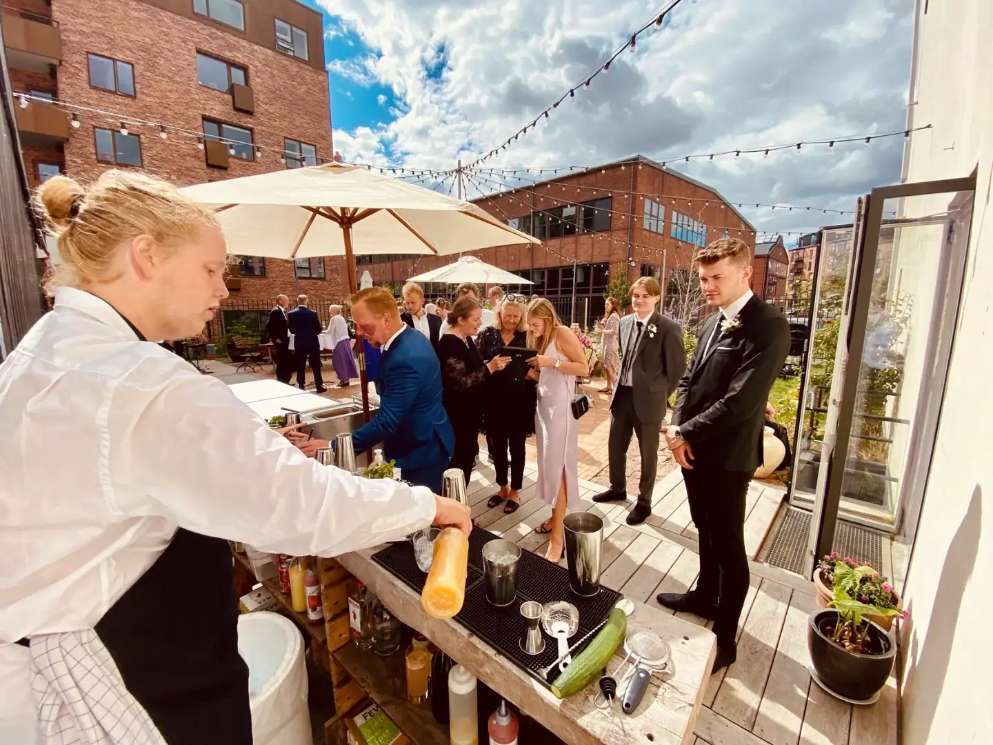 En bartender fra Copenhagen Crew serverer drinks fra en udendørs bar til gæster på en tagterrasse.